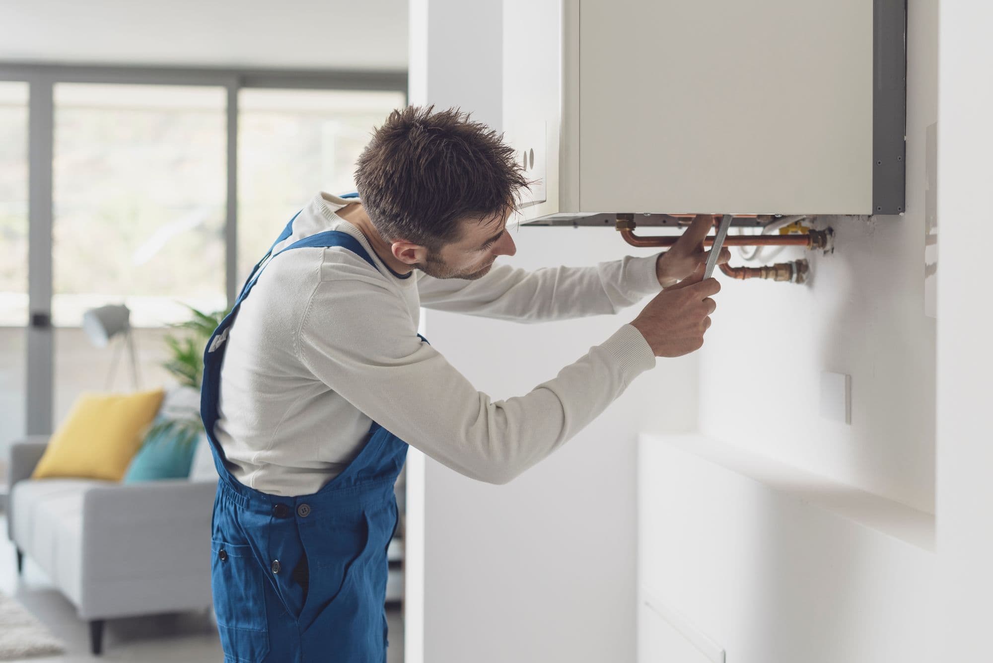 Heating engineer fitting the pipework under a new wall-mounted boiler in a living room