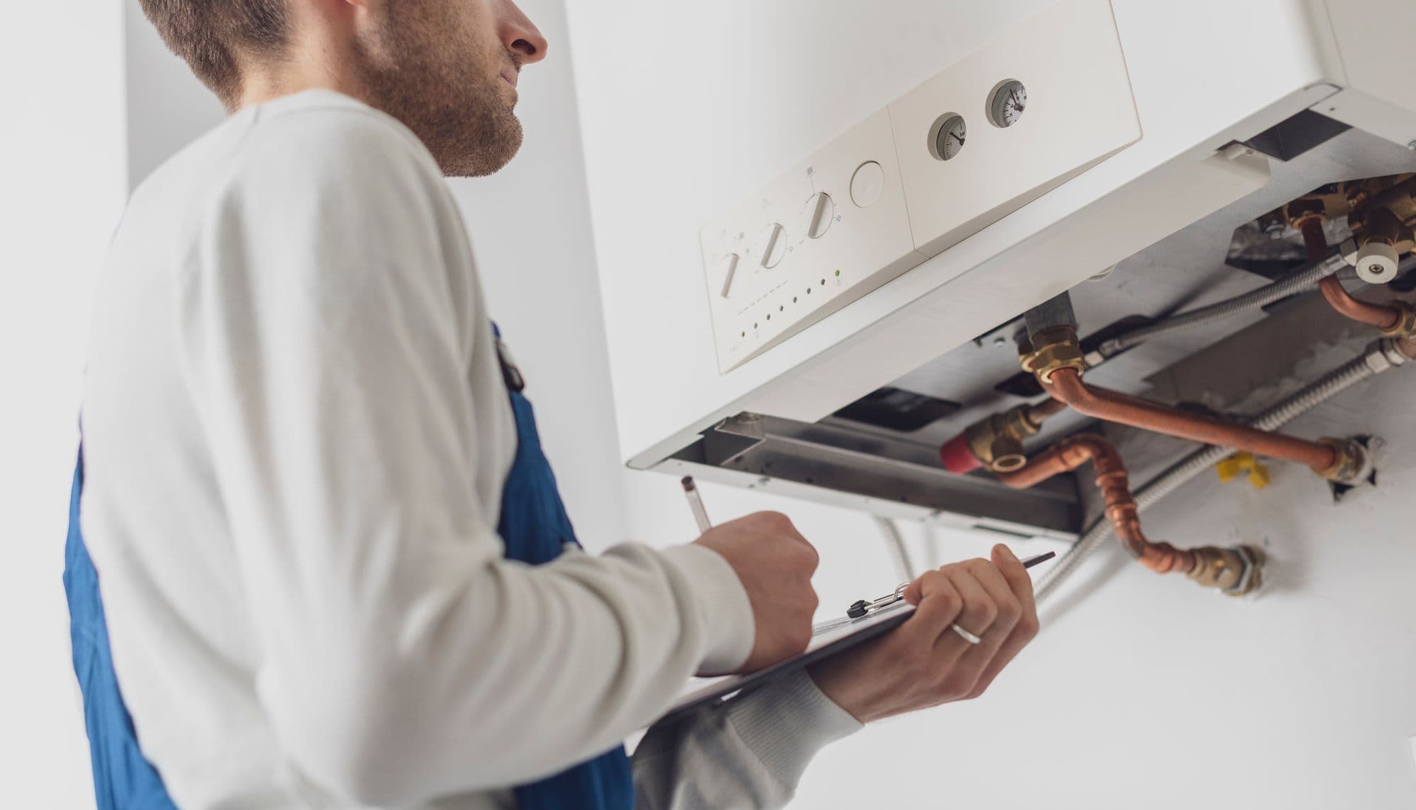 Engineer recording readings on a clipboard while servicing a boiler