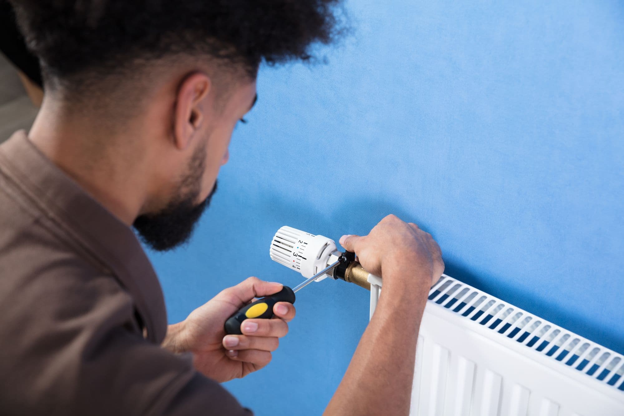 Plumber fitting a thermostatic radiator valve with a screwdriver