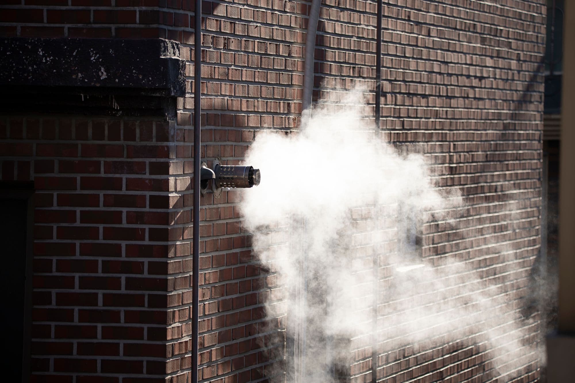 Boiler flue on a brick wall releasing a plume of condensation on a cold day