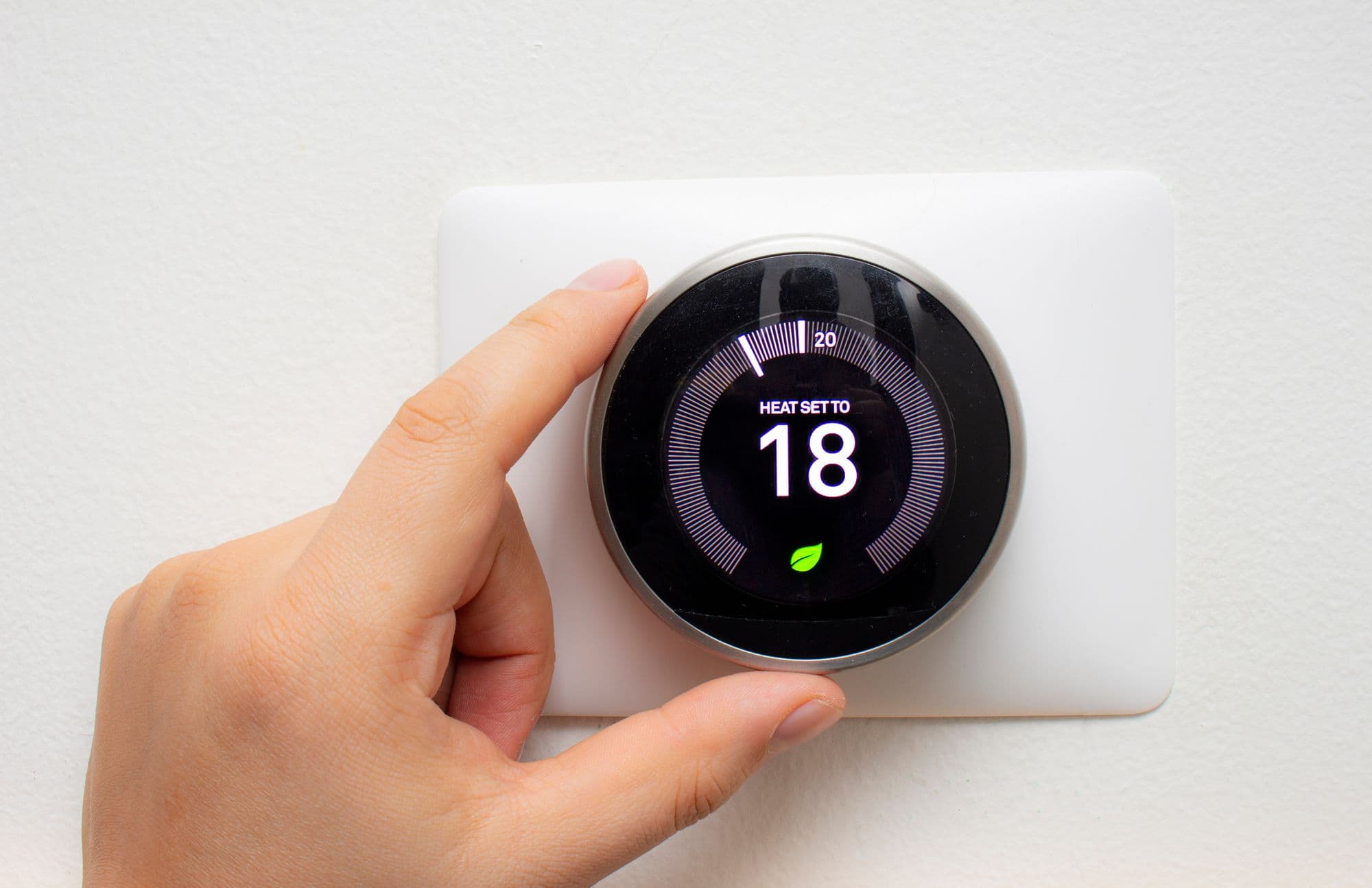 Hand turning a round smart thermostat set to 18 degrees